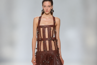 Mannequin portant une robe marron à lanières de cuir et ornements métalliques lors du défilé Jean Paul Gaultier printemps-été 2027 à Paris.