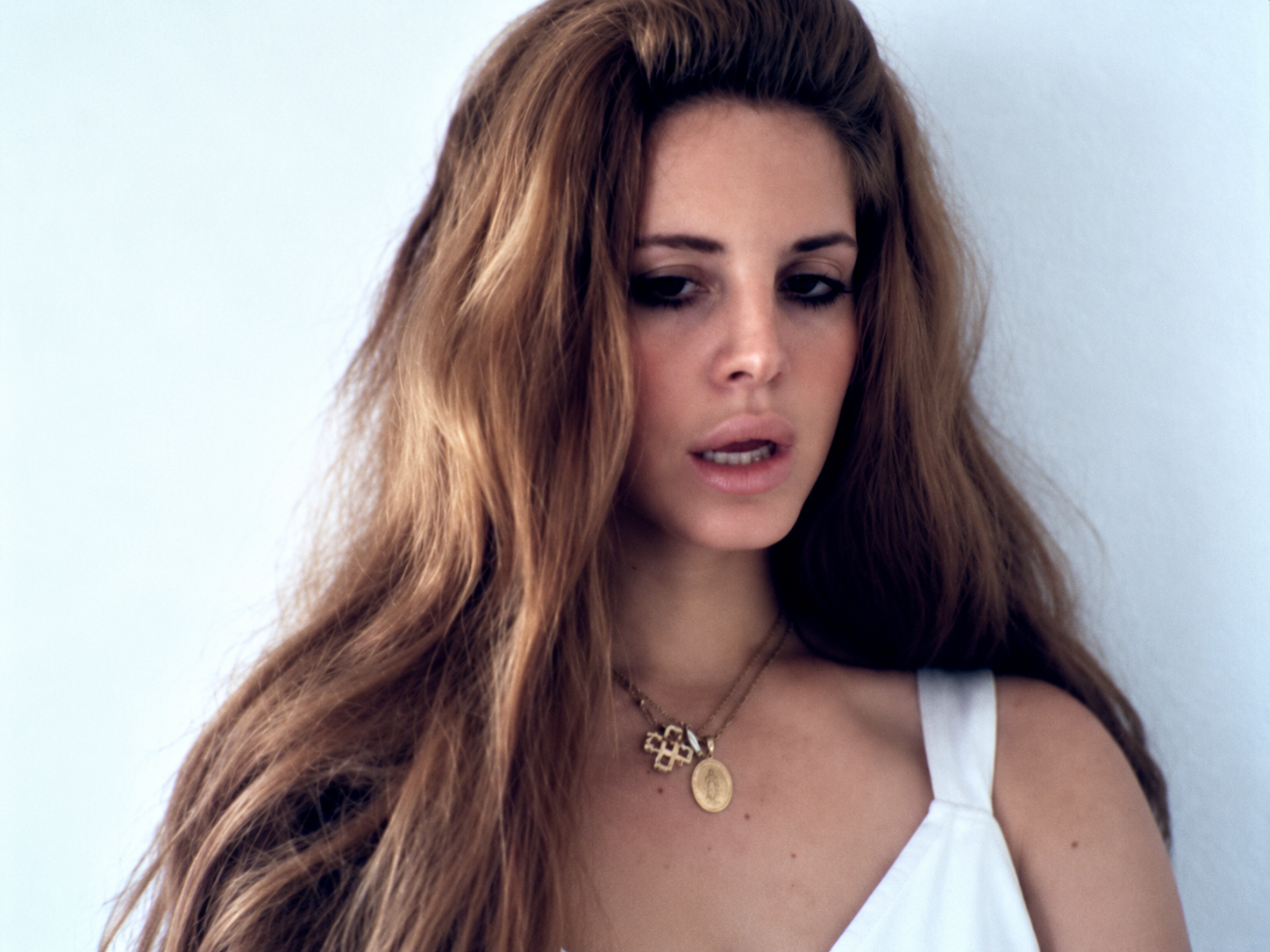 Lana Del Rey dans le clip Video Games, cheveux longs volumineux, maquillage rétro et robe blanche, dans une esthétique vintage.