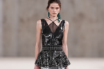 Mannequin du défilé Lanvin printemps-été 2027 portant une longue robe noire à sequins argentés, taille structurée, basque géométrique et boucles d'oreilles vertes.