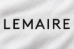 Logo Lemaire brodé en fil noir sur un tissu blanc en coton, détail textile de la maison de mode française.