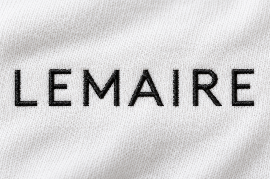 Logo Lemaire brodé en fil noir sur un tissu blanc en coton, détail textile de la maison de mode française.