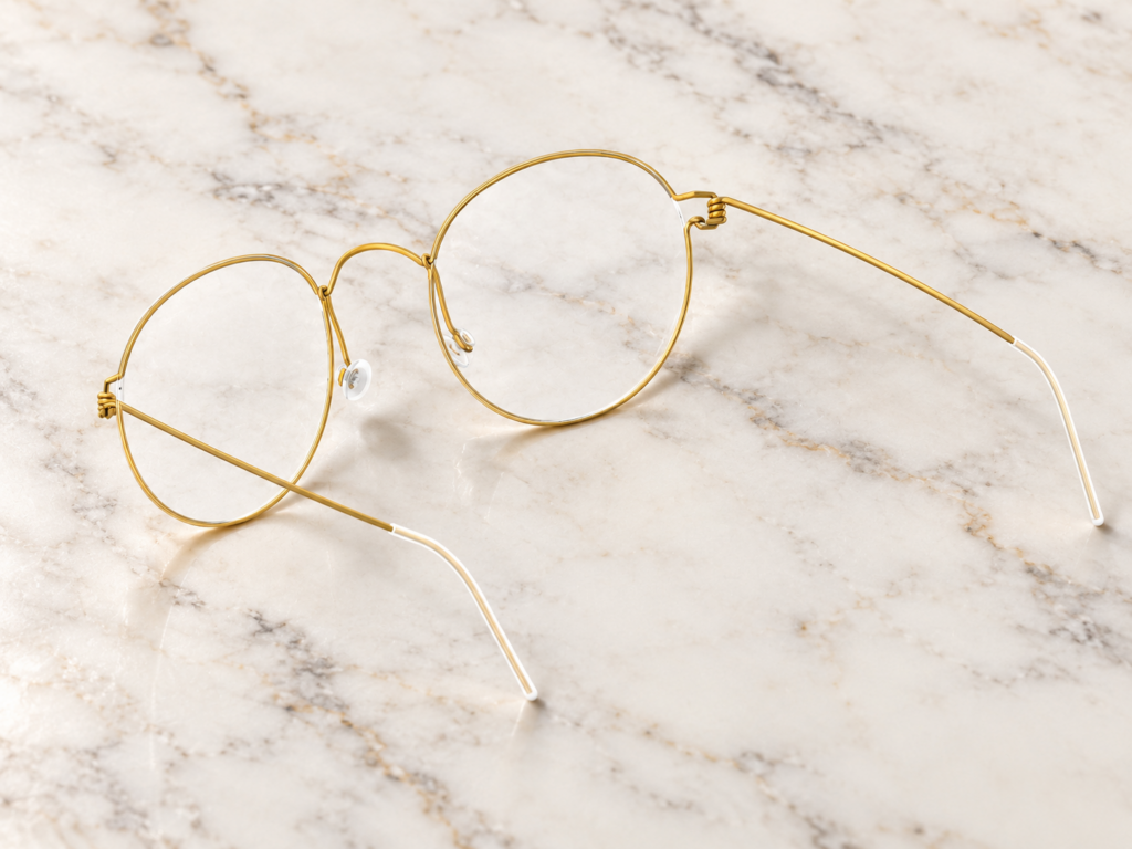 Lunettes de vue LINDBERG Air Titanium Rim en titane doré, à monture ronde et charnières en spirale, posées sur une plaque de marbre clair.