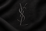 Logo YSL Yves Saint Laurent brodé en noir sur un tissu noir, détail du monogramme historique aux lettres entrelacées.