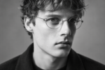 Jeune homme aux cheveux ondulés portant des lunettes Lindberg Air Titanium Rim à monture métallique fine et ronde.