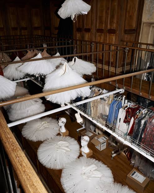 Tutus blancs de ballet disposés sur des supports, portants de costumes et boiseries dans un espace de stockage.
