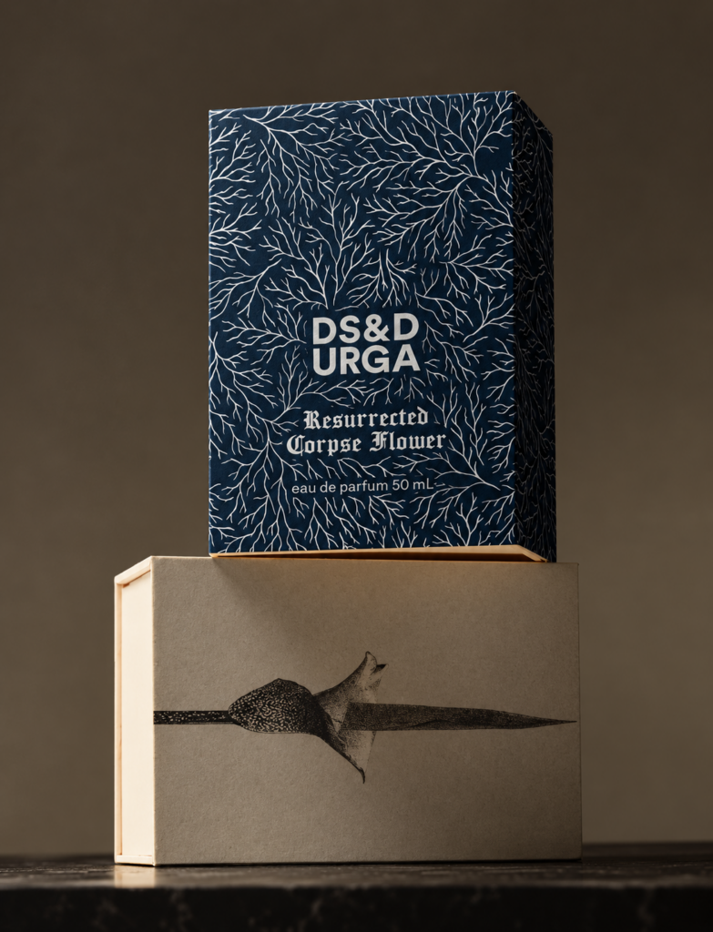Boîte bleue du parfum Resurrected Corpse Flower de D.S. & Durga, décorée de motifs végétaux blancs, posée sur un coffret beige illustré.