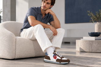 Jeune homme portant les sneakers COERENZA de Jerome Ruggiero, un pantalon blanc et un polo bleu gris dans un intérieur moderne.