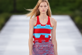 Silhouette rouge et bleu turquoise du défilé Stella McCartney printemps-été 2027 à la Paris Fashion Week, sur fond de podium flouté.