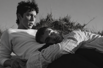 Troye Sivan et un jeune hommes allongé dans les dunes, dans une scène en noir et blanc d’un clip de Troye Sivan.