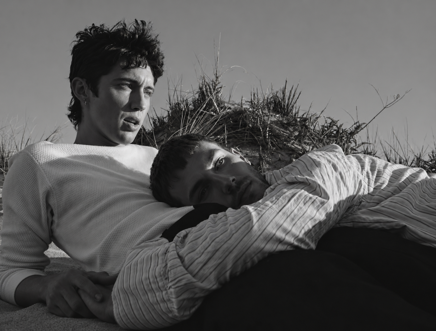 Troye Sivan et un jeune hommes allongé dans les dunes, dans une scène en noir et blanc d’un clip de Troye Sivan.
