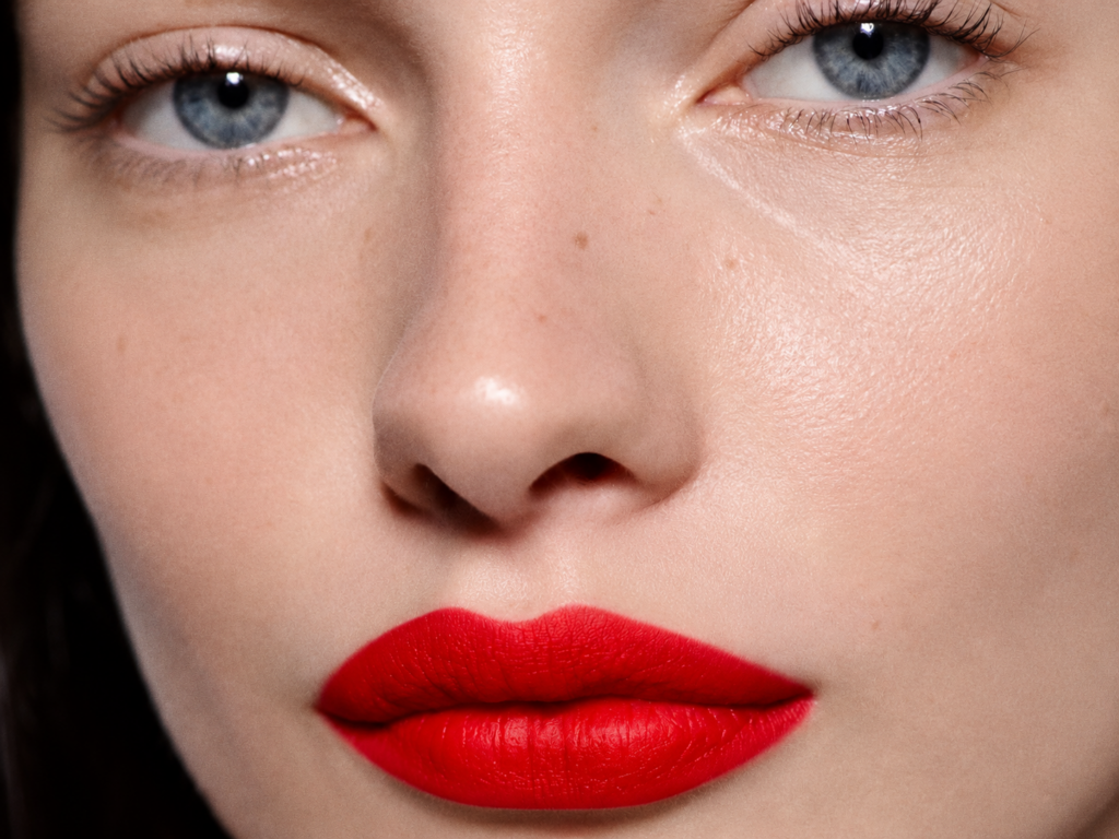 Gros plan sur les lèvres rouge vif d'un mannequin aux yeux bleus, illustrant la teinte Coquelicot du rouge à lèvres Rouge Victoria de Victoria Beckham Beauty.
