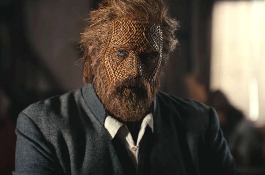 Alexander Skarsgård dans Wicker, le visage recouvert d’un masque en osier tressé, vêtu d’un costume sombre.