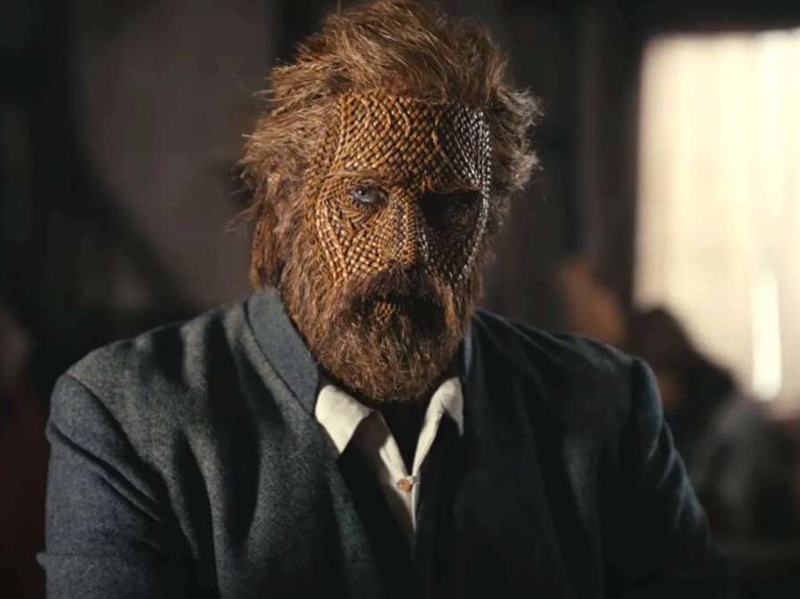 Alexander Skarsgård dans Wicker, le visage recouvert d’un masque en osier tressé, vêtu d’un costume sombre.