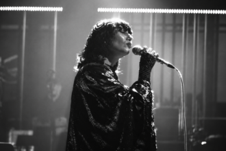 Karen O, chanteuse des Yeah Yeah Yeahs, interprète un morceau au micro dans une scène en noir et blanc du court-métrage Hidden in Pieces.